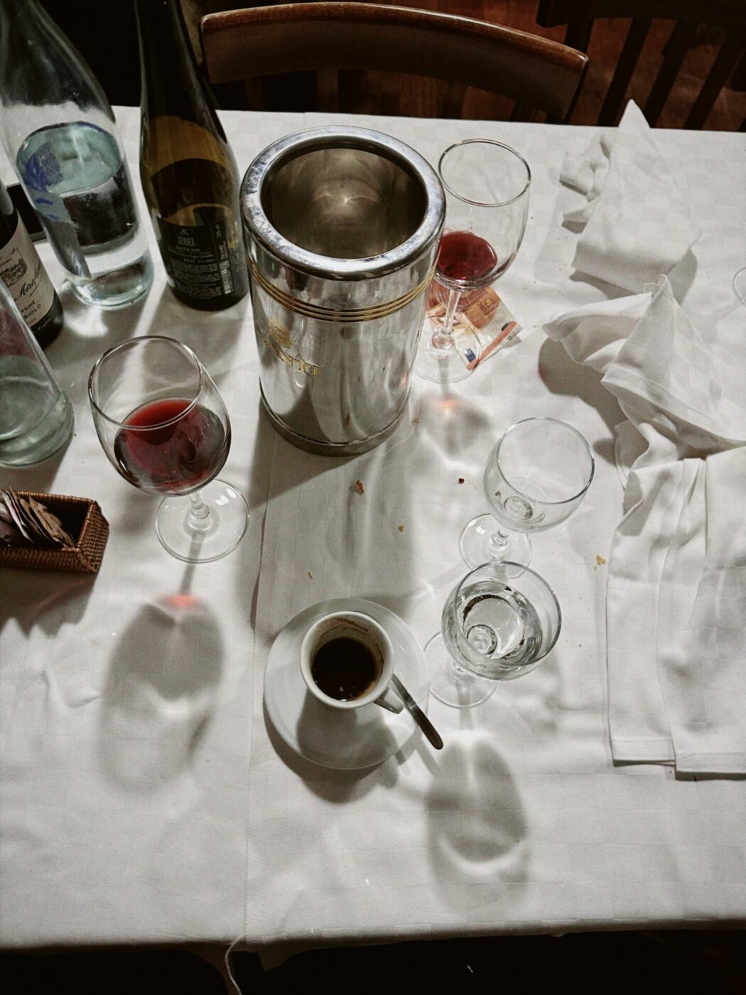 Photo of the end of a dinner table at a restaurant with half-finished glasses of wine, water and espresso