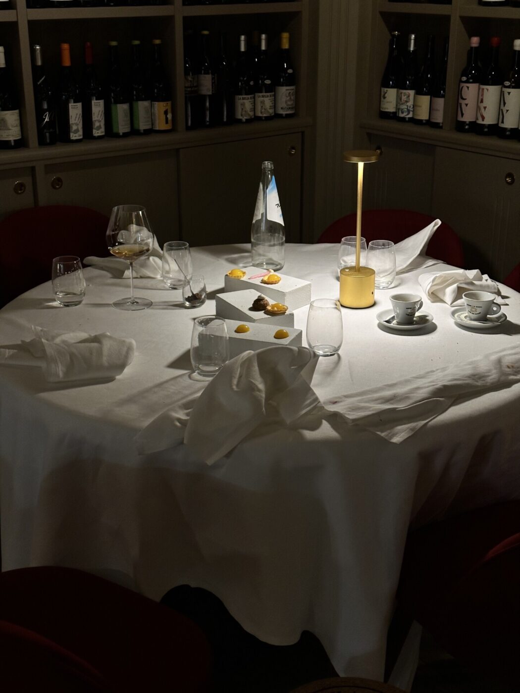 an intimately lit circular table in the corner of a fine dining establishment with empty wine glasses and white napkins
