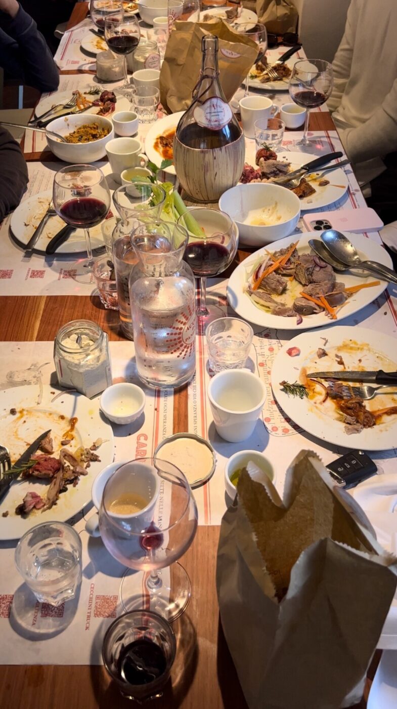 photo of a large messy dinner table at a restaurant with bits of remaining food and wine