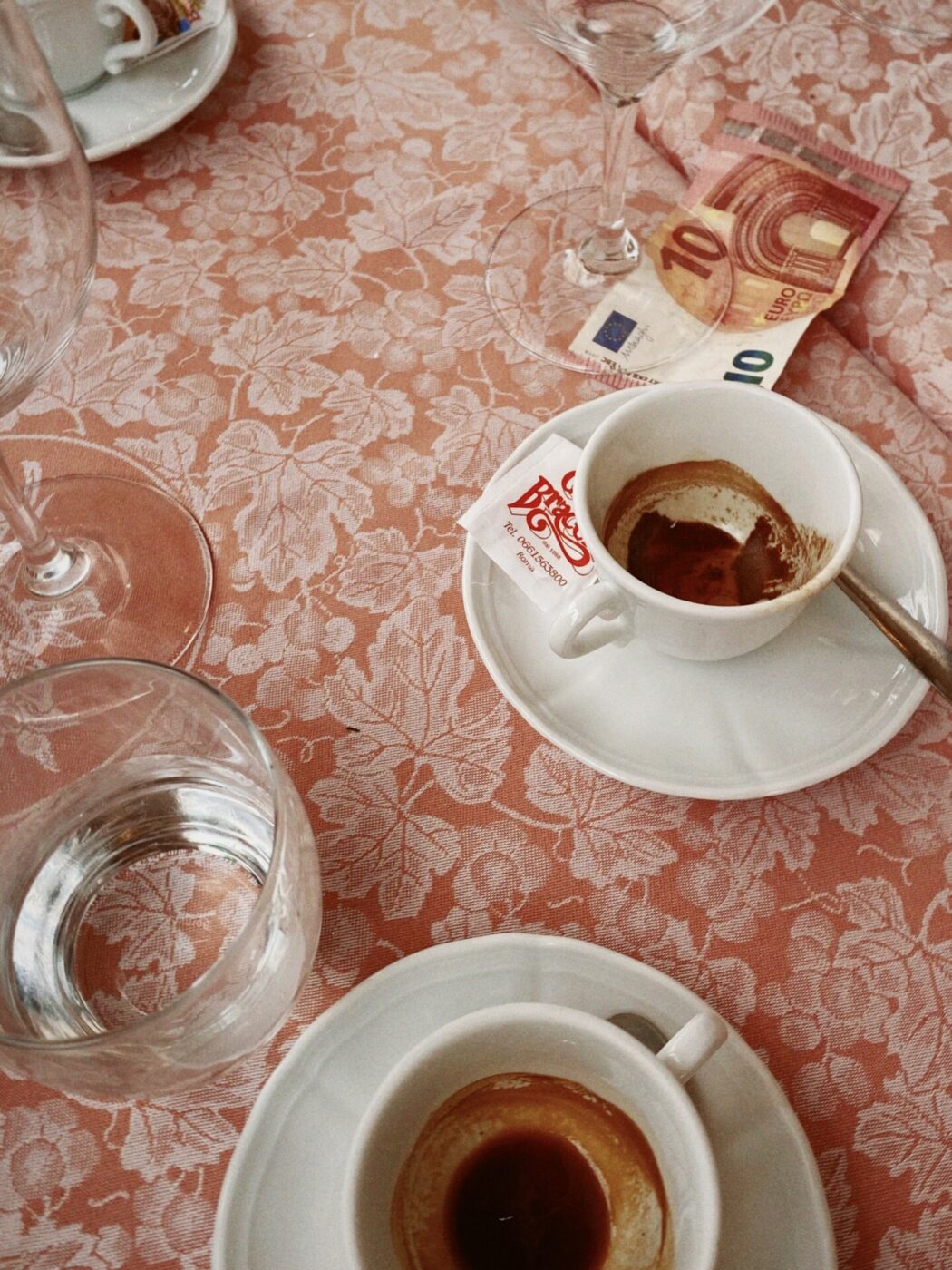 empty espresso cups and a 10 euro bill on light red tablecloth with a grape and grape leaf pattern