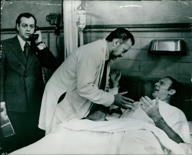 A vintage photo of a doctor talking with a bedridden patient in a hospital while a man talks on the phone behind him