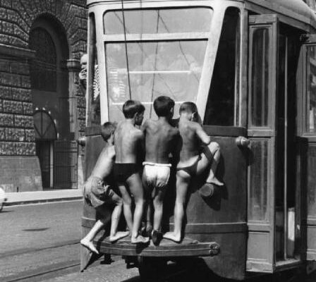 black and white photo of four boys in shorts on the back of a tram