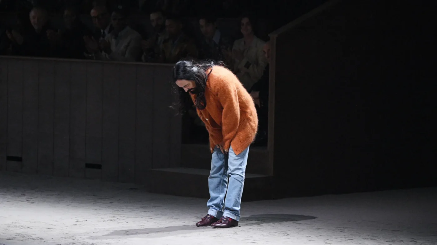 Alessandro Michele wearing an orange sweater and blue jeans bending over