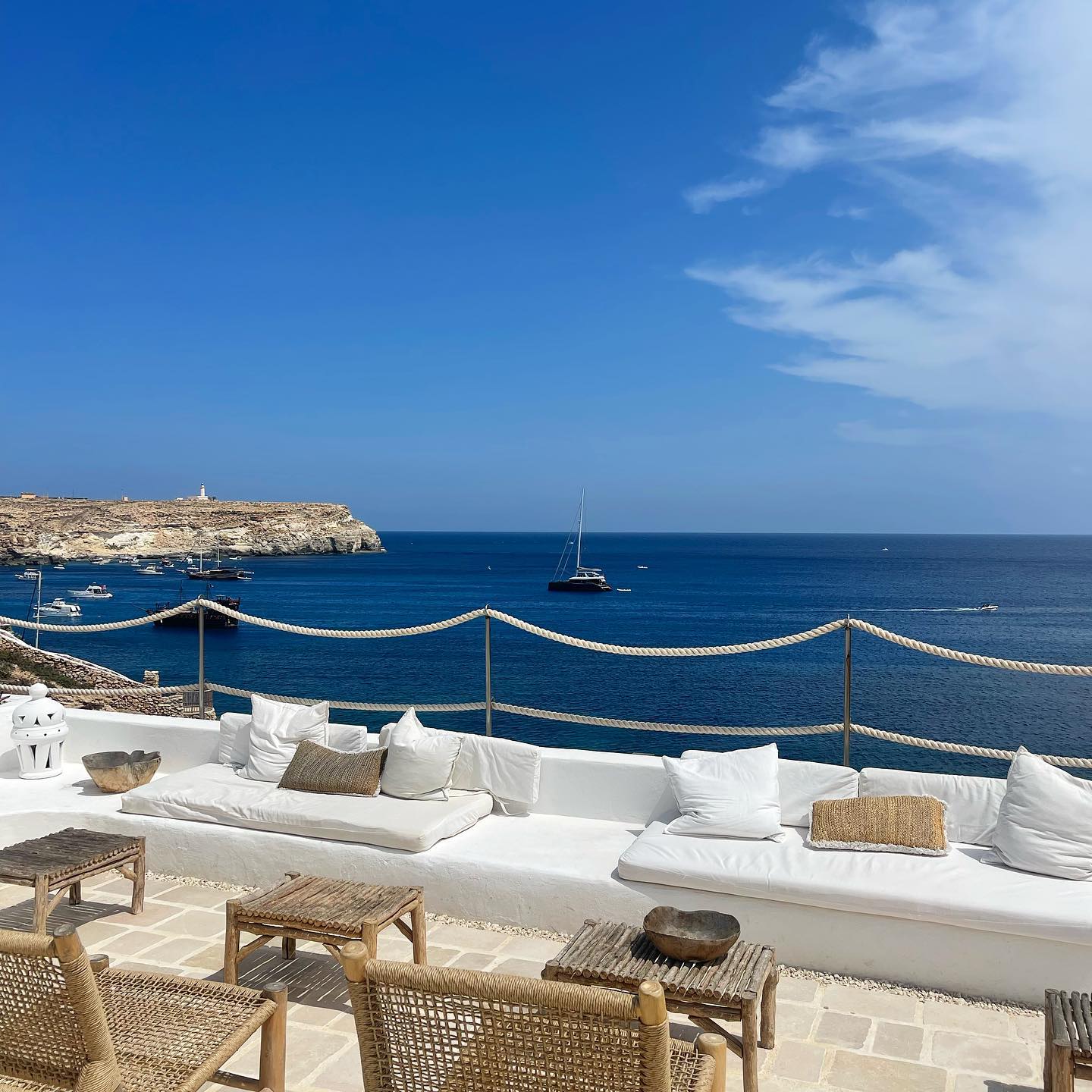 Courtesy of La Calandra - a terrace with wooden tables and chairs and white couches overlooking the sea in Sicily