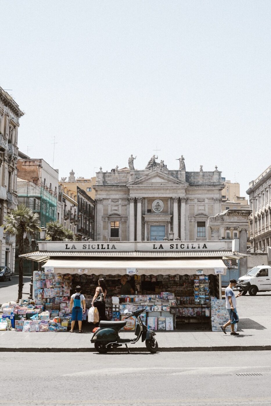 a photo of a newsstand called "La Sicilia" in a piazza in Sicily with a vespa parked out front