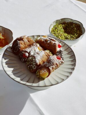 a sunny plate of 5 short cannoli next to a bowl of ground pistachios