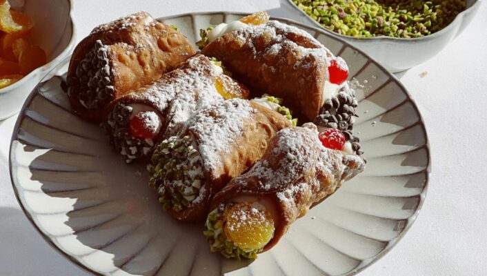 a sunny plate of 5 short cannoli next to a bowl of ground pistachios