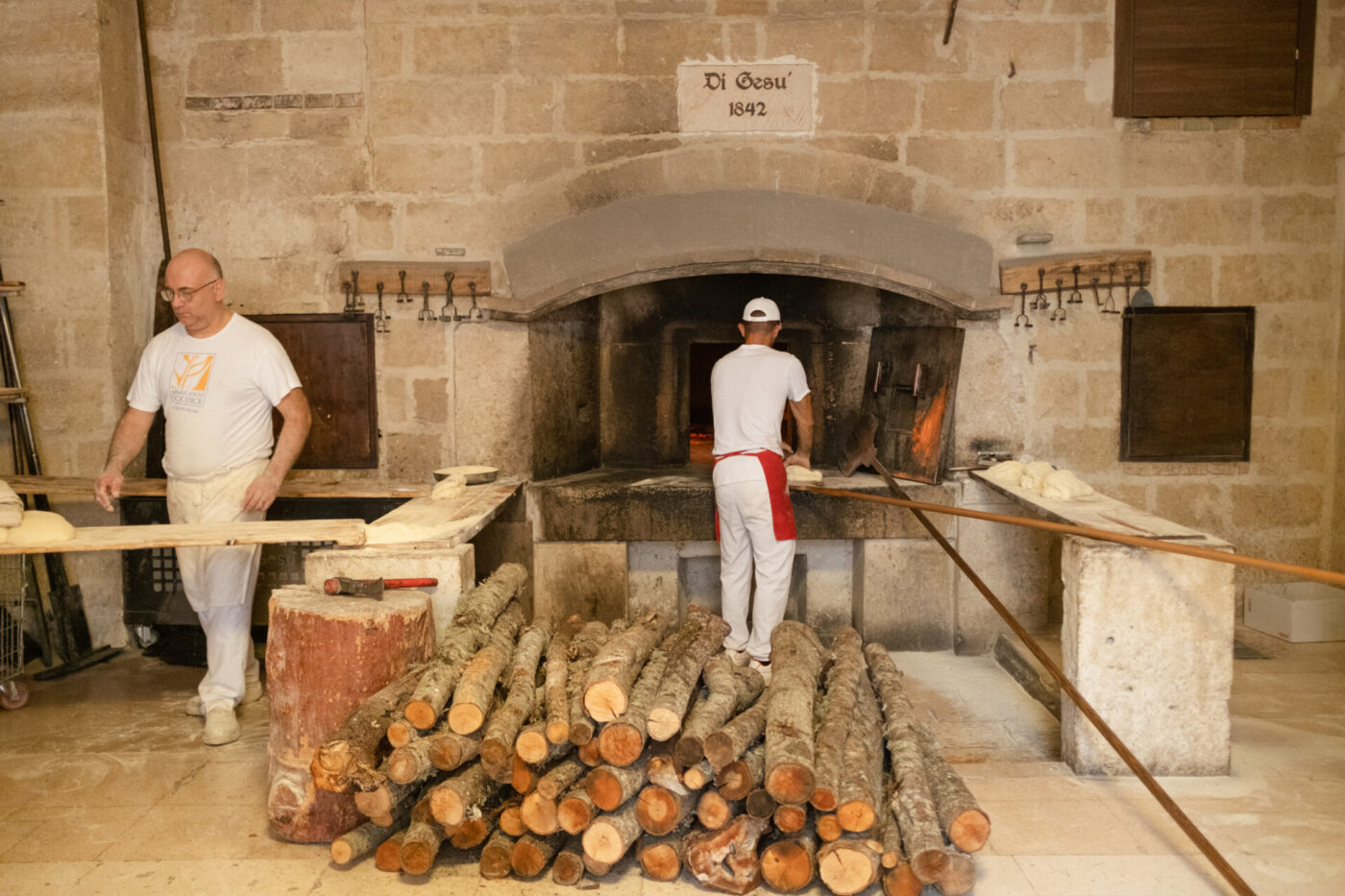 two men stoking the wood fired oven with stacks of logs out front at Panificio Di Gesù