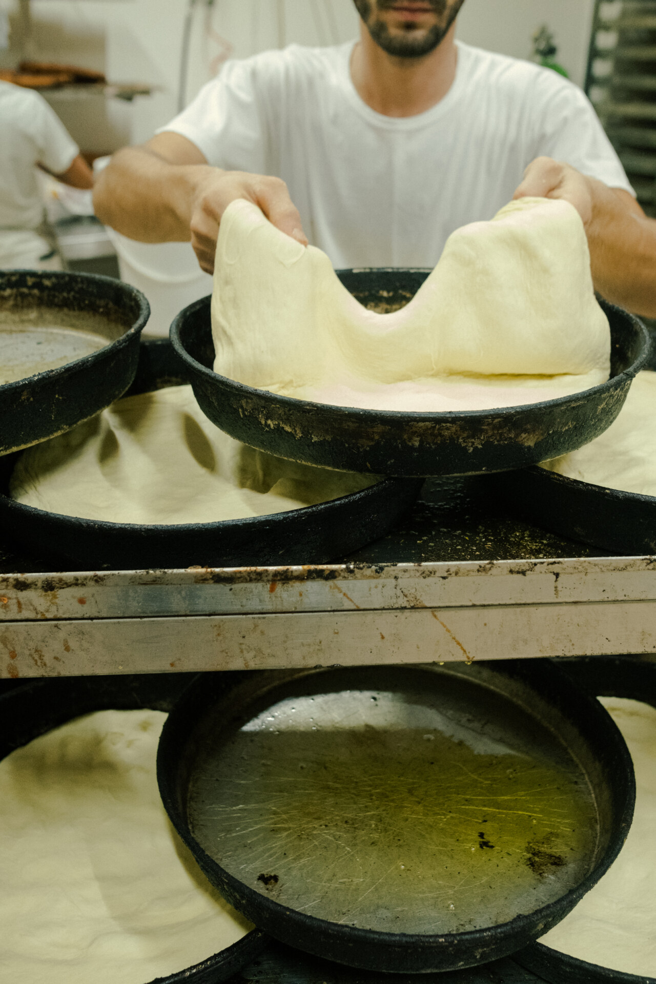 a man working with pizza dough in round, deep pans at Panificio Di Gesù