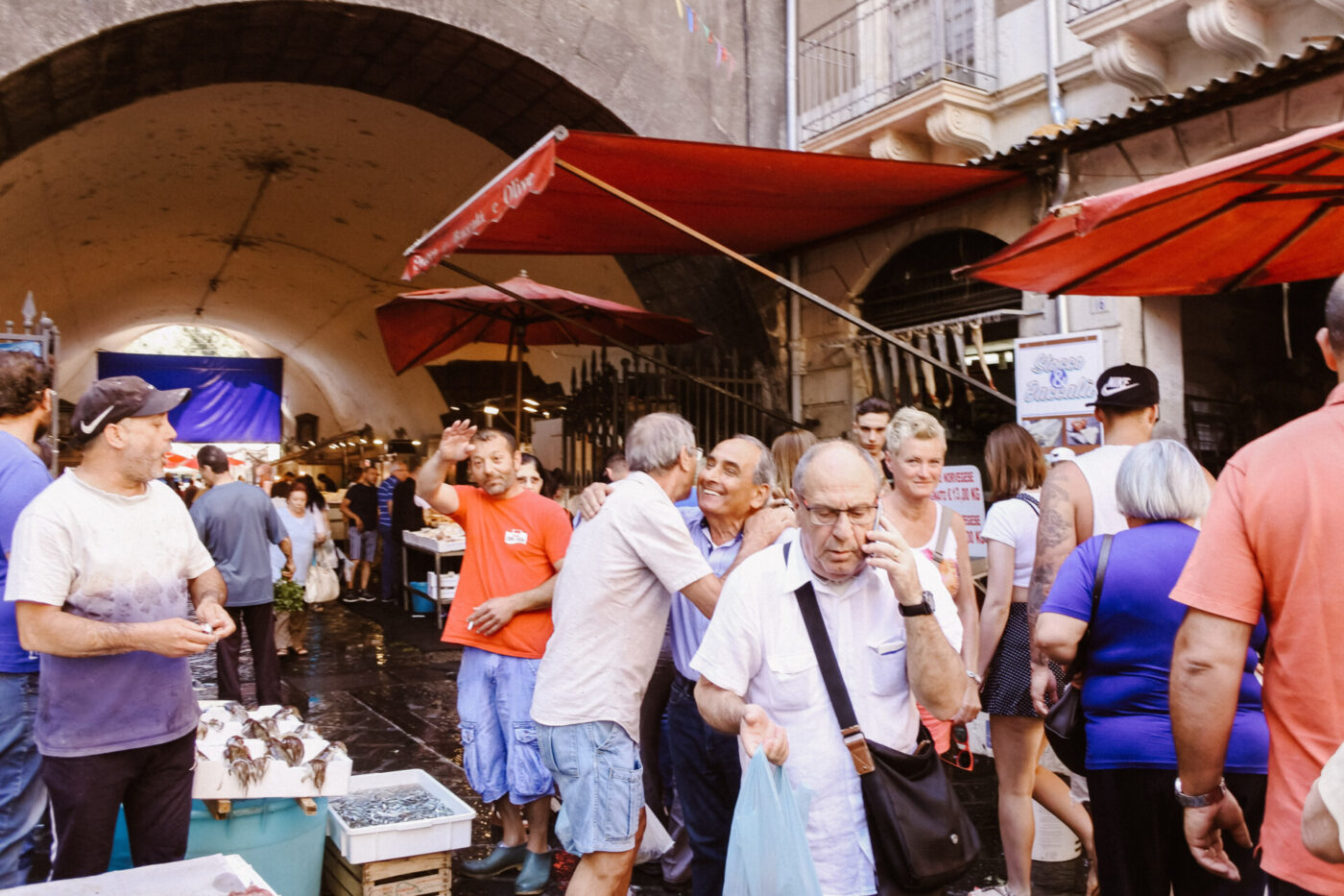 Photography by Gina Spinelli of a bustling market in Catania with patrons hugging and waving