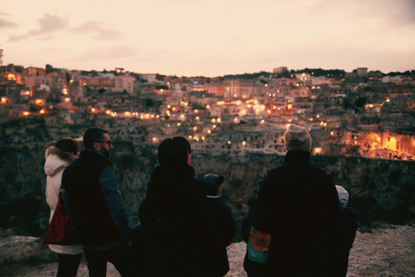 a photo of four people from the back in the foreground and the lit up city of Altamura in the background