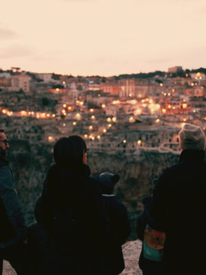 a photo of four people from the back in the foreground and the lit up city of Altamura in the background