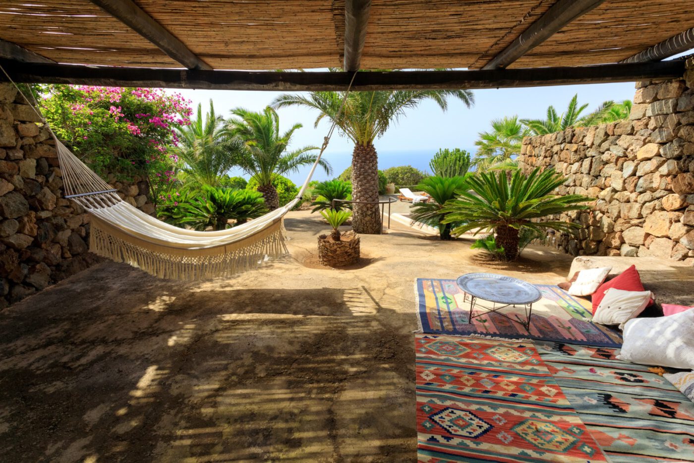 Kardibà resort in Pantelleria; a hammock and nice mats on a patio with palm trees in the background