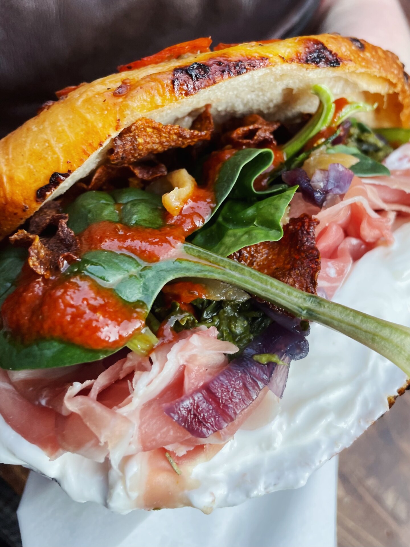 a close up of an overstuffed panino filled with meat and spinach and a a red sauce