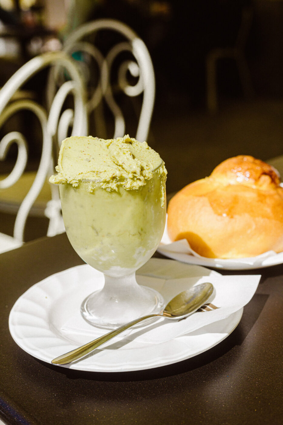 Comis Ice Cafe - overflowing cup of pistacio gelato with a brioche on a table outside