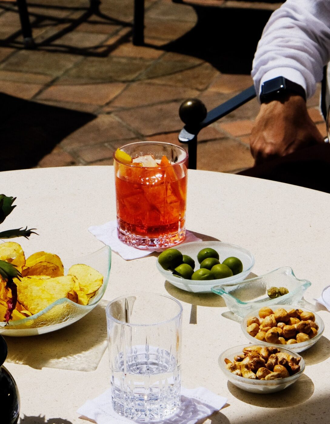 am elegant photo of a table at aperitivo with green olives, peanuts, an orange spritz in a highball glass, and potato chips