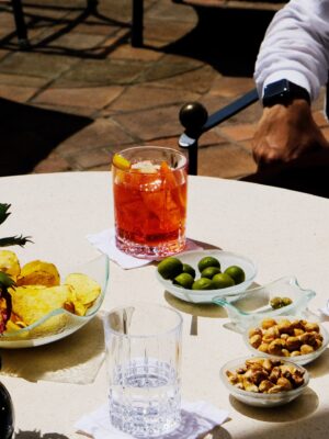 am elegant photo of a table at aperitivo with green olives, peanuts, an orange spritz in a highball glass, and potato chips