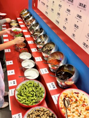 people getting sauce and toppings from a bar at bashifu hotpot