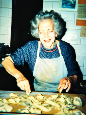 photo by Roberto Beragnoli: an Italian grandma wearing a white apron in a white tile kitchen making homemade pasta
