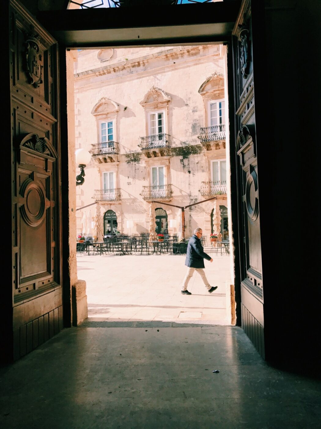 a photo taken in Ortigia through an open church doorway into a piazza and a man walking by