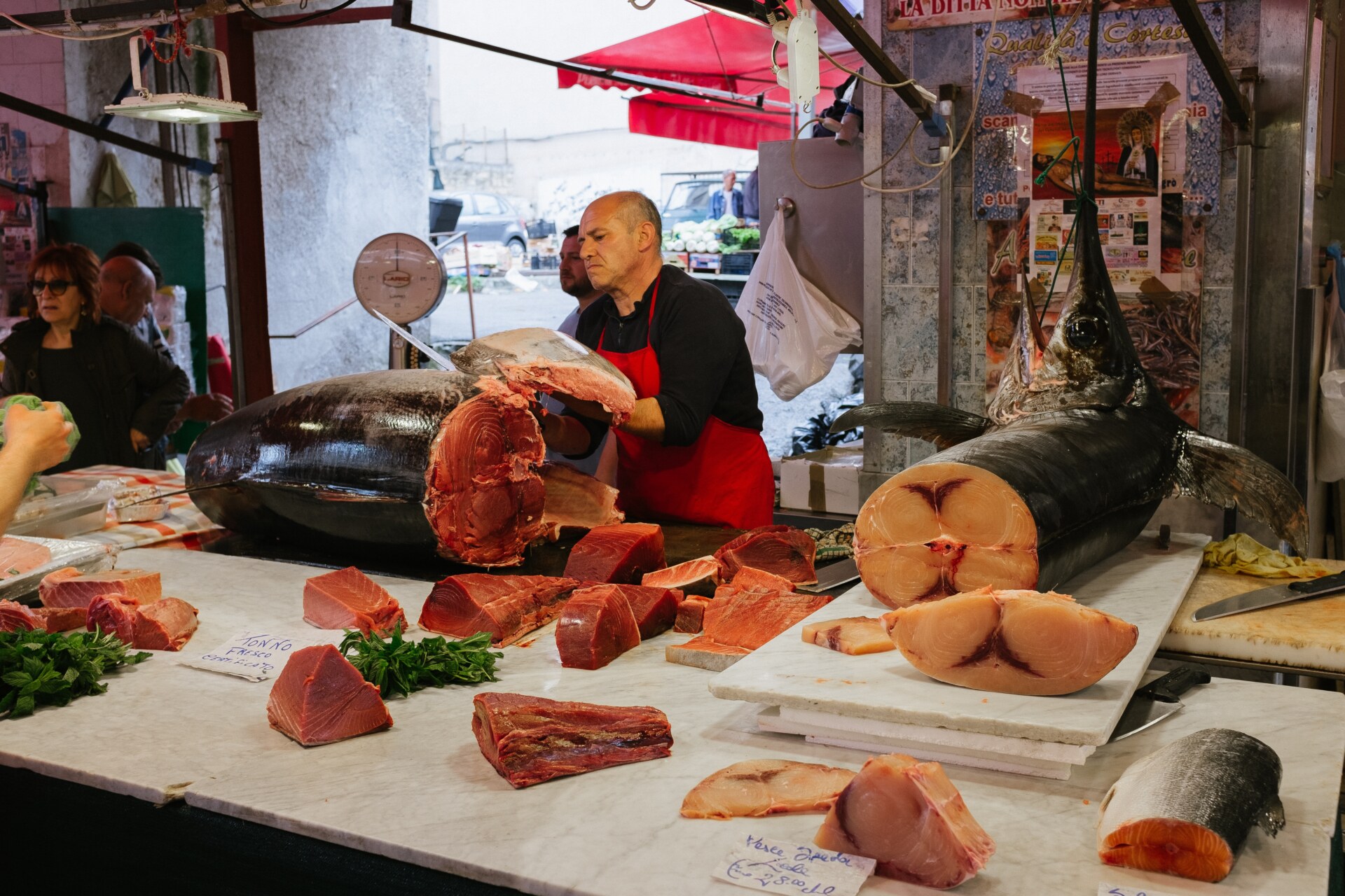 a fishmonger butchering a giant fish behind a white counter with other cuts of fish and selling it at Palermo's Ballarò market