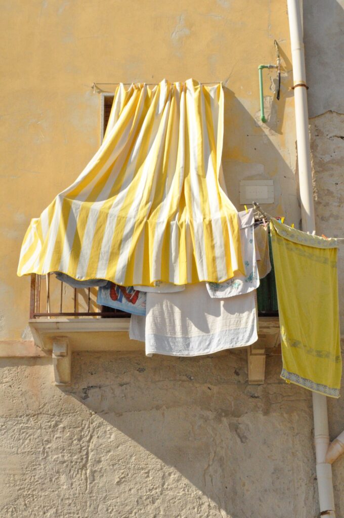 a balcony in Ortigia Sicily with clothes hanging on the line and a yellow and white stripped curtain draping over the balcony