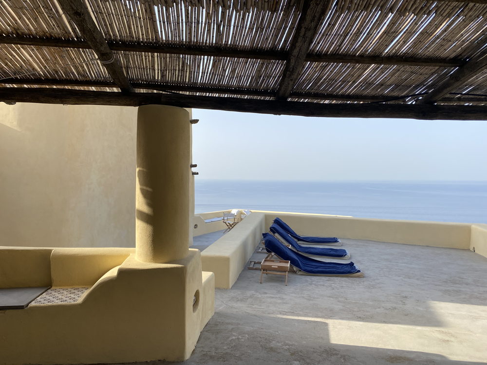 a clean white terrace with blue lounge chairs at Casa G in Sicily overlooking the sea