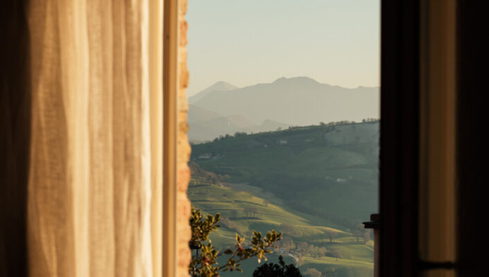 a view out the sunny window of a curving road through picturesque hills in Italy