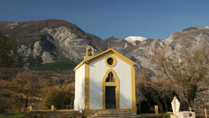 Civitella in Maiella - a small white church with yellow trim standing alone at the foot of mountains
