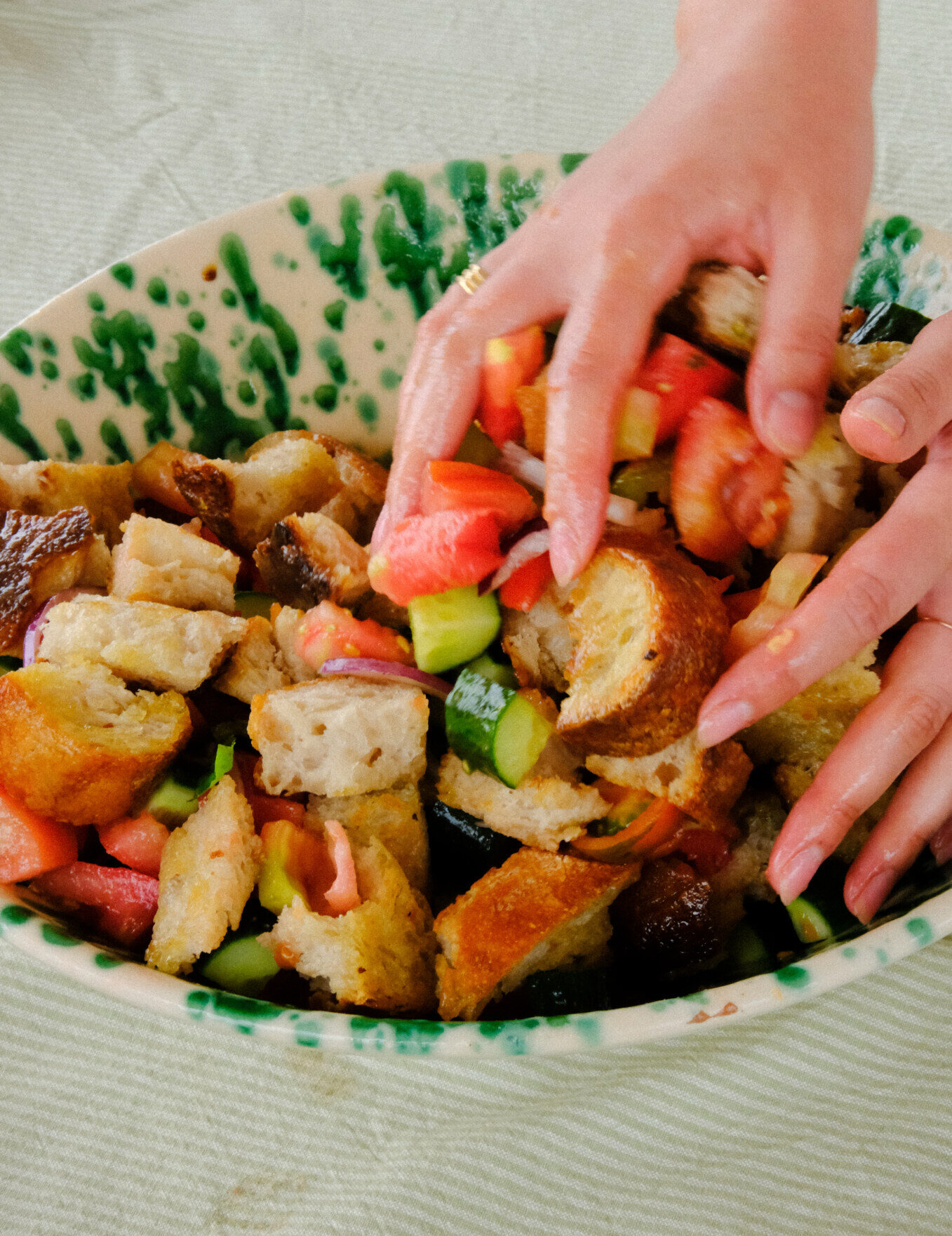 a woman tossing a panzanella salad with her hands