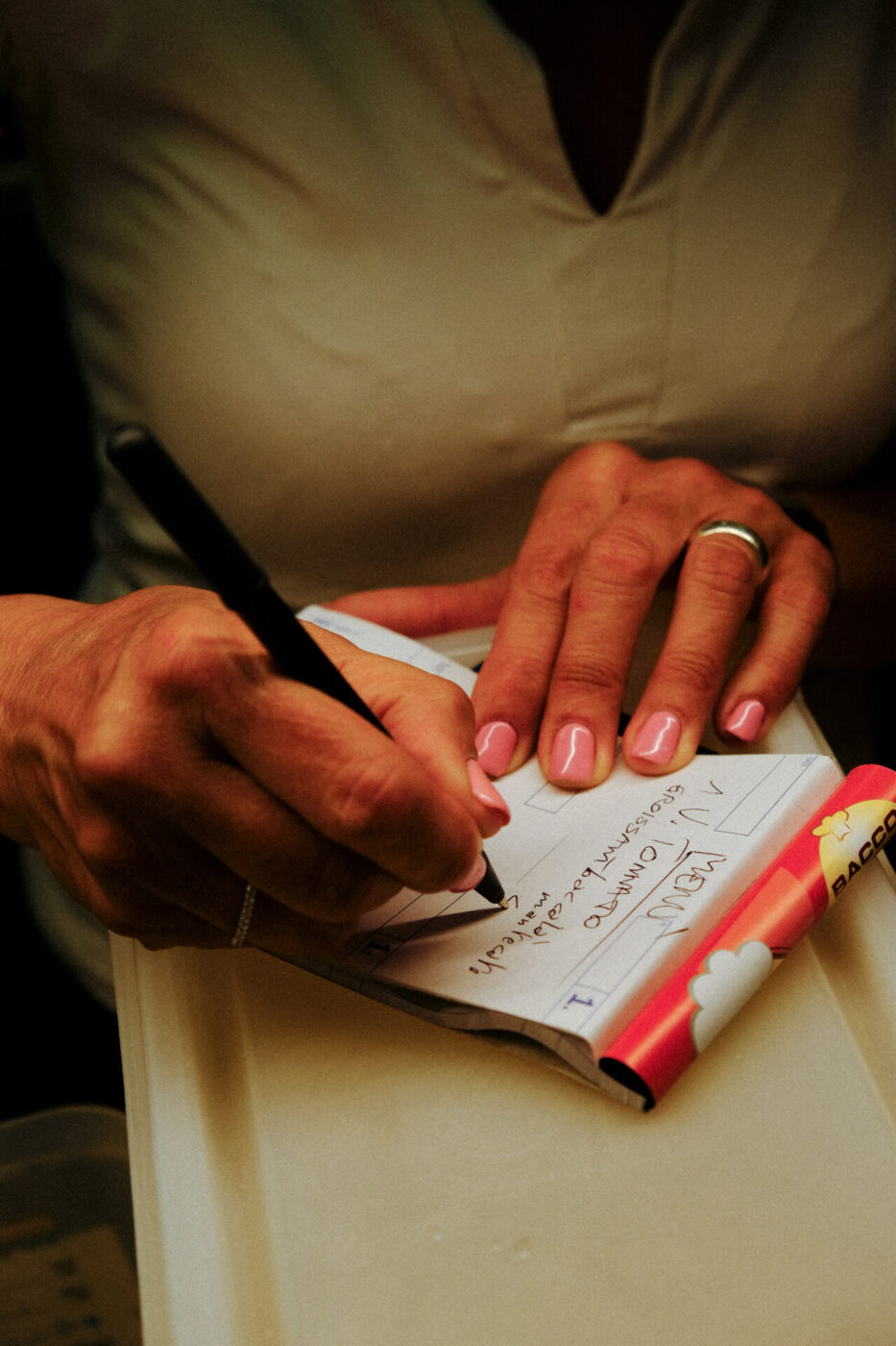 a close up of a woman with light pink nails writing down an order at Cibreo in dim lighting