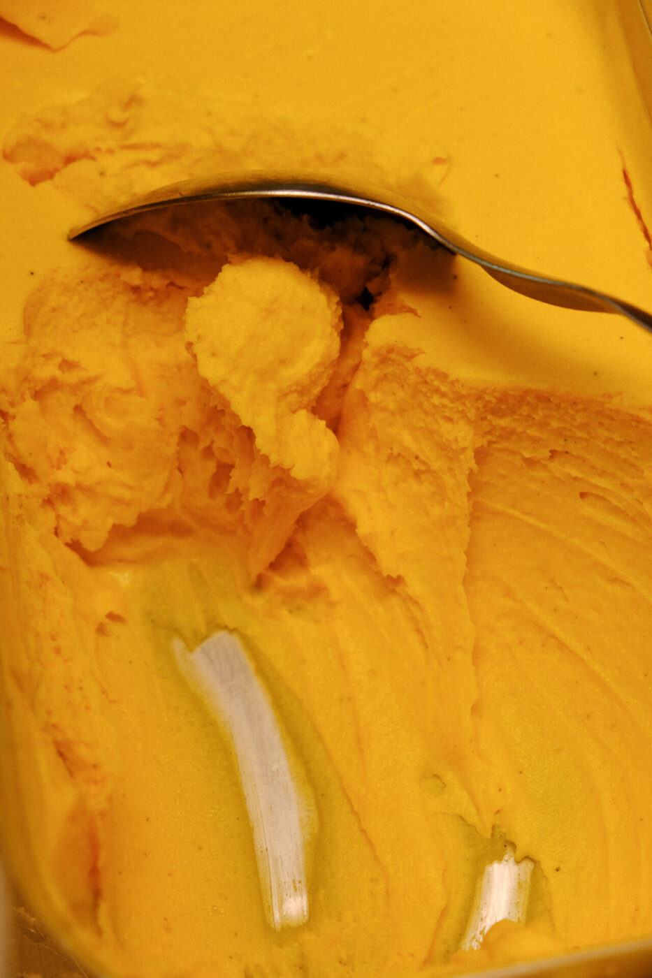 a close up of a spoon scooping an orange colored gelato