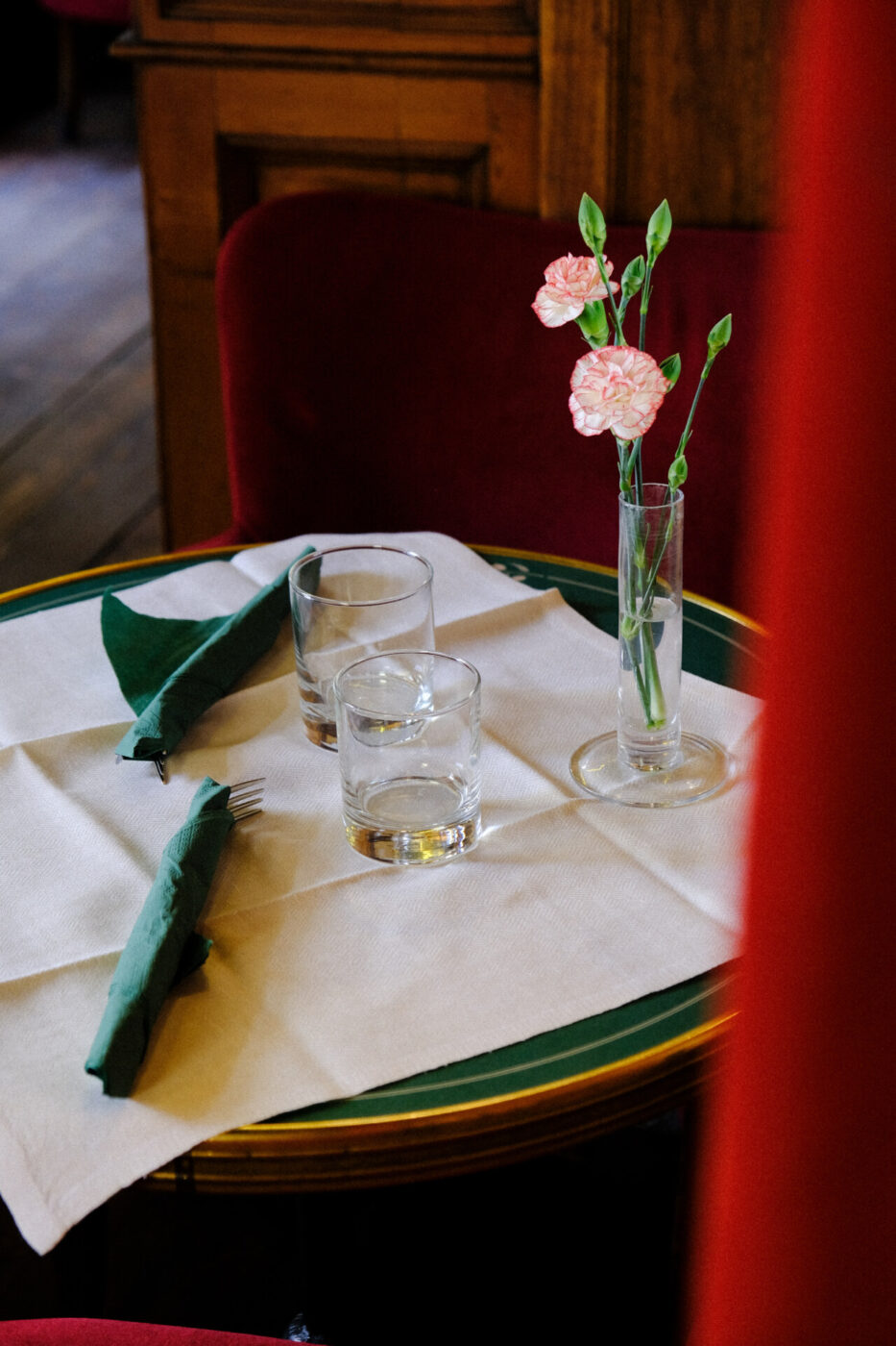 a dark green table for two set at Cibreo with a white table cloth and a small vase of pink flowers