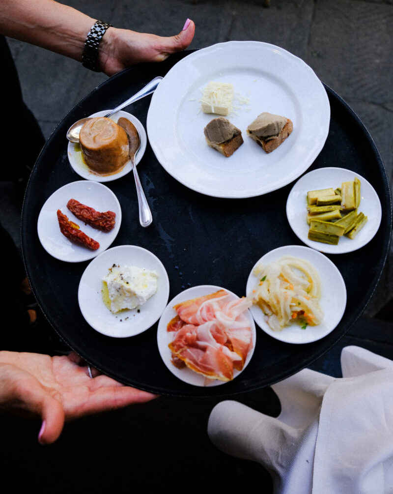 a waiter carrying a black tray at Cibreo with 7 different white plates filled with Antipasti