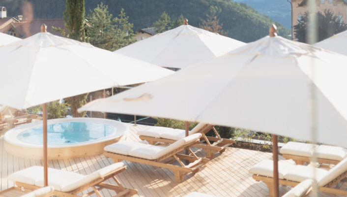 the sundeck at Schgaguler Hotel with white sunbeds, a whirlpool, and tan umbrellas against the mountains