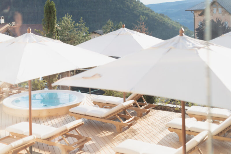 the sundeck at Schgaguler Hotel with white sunbeds, a whirlpool, and tan umbrellas against the mountains
