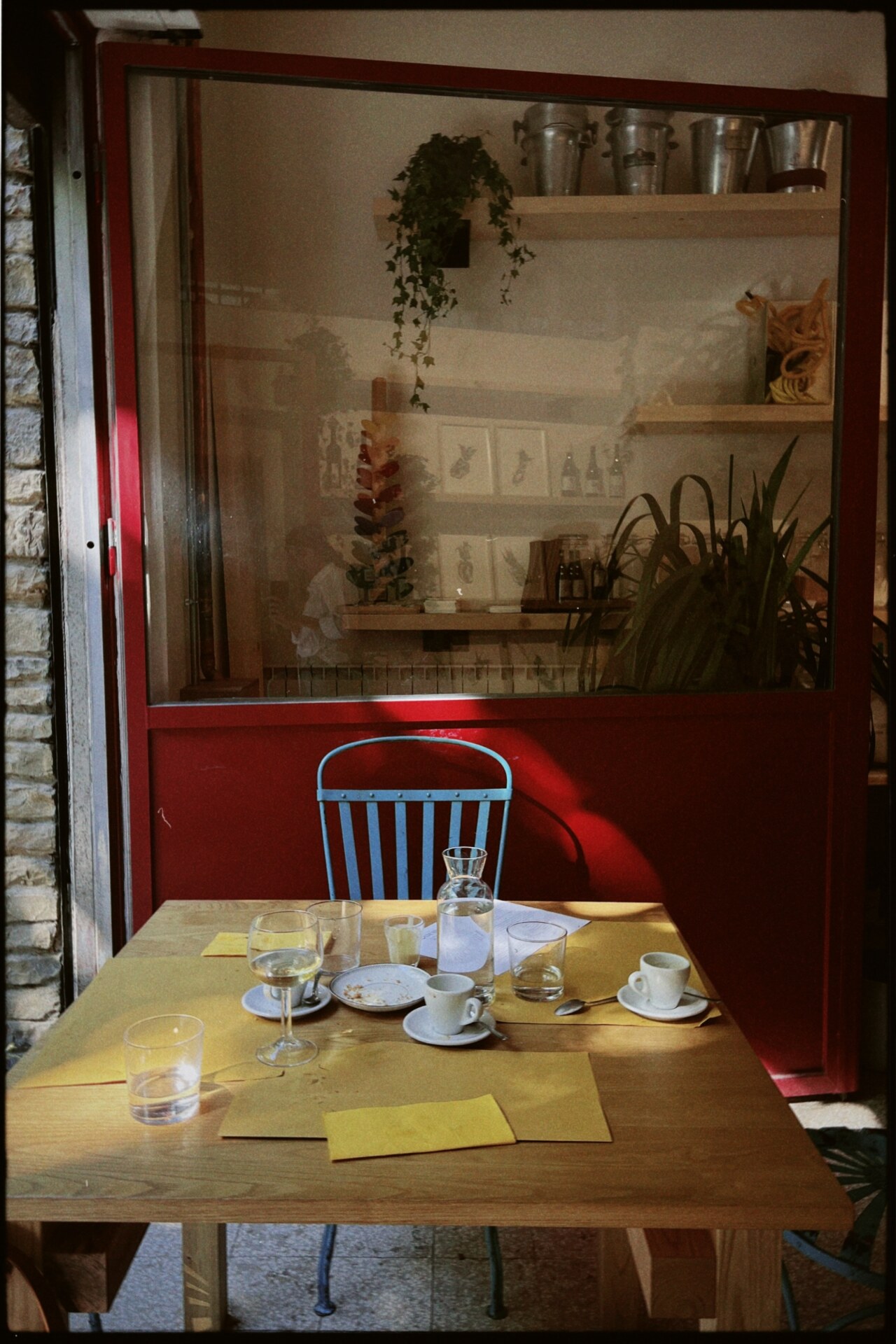 an empty table against the window at a cafe in Florence with empty espresso cups and wine glasses and a red wooden chair at c-ucina