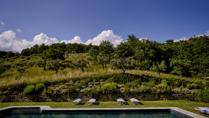 the pool at Le Caviere with four lounge chairs on the side below a rolling green hill and blue sky