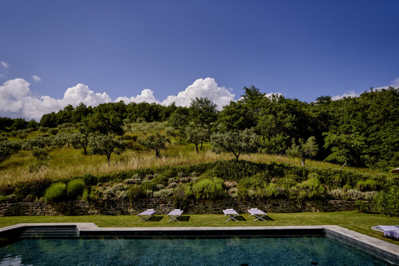 the pool at Le Caviere with four lounge chairs on the side below a rolling green hill and blue sky