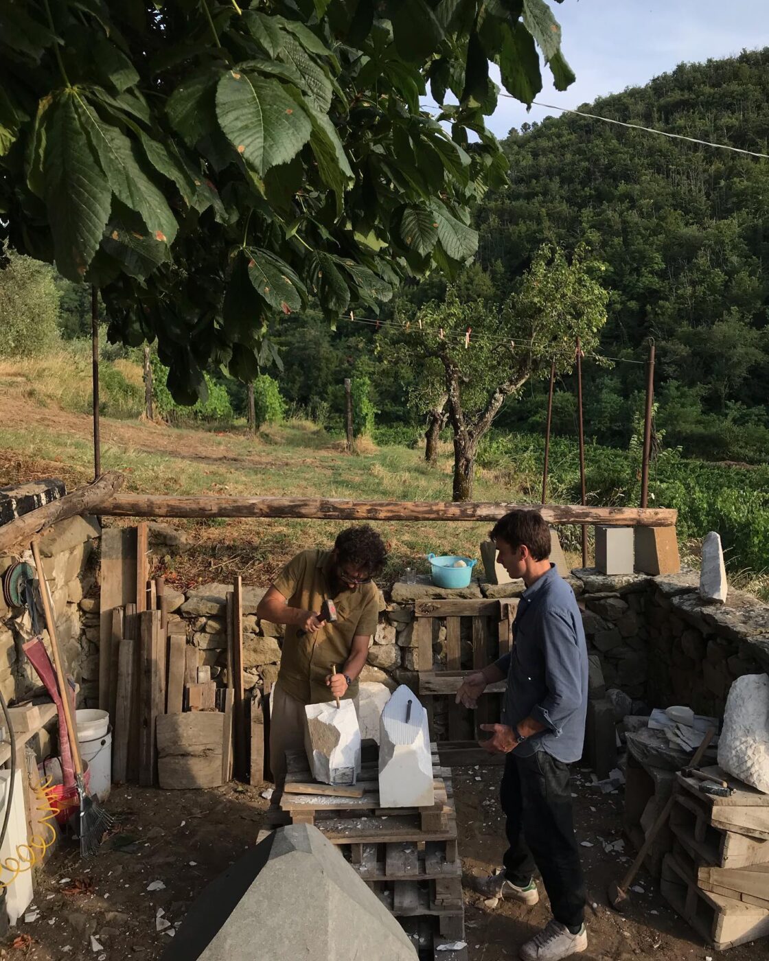 Lorenzo Brinati and another man working out on a hillside at golden hour sculpting something out of marble