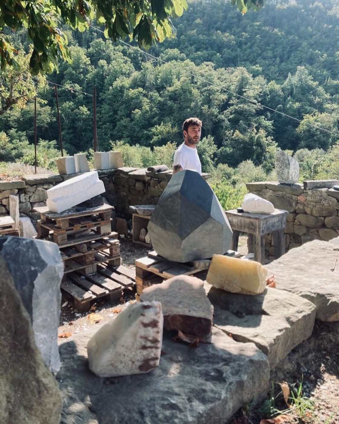 sculptor Lorenzo Brinati standing on a hillside around large pieces of rocks he's going to sculpt