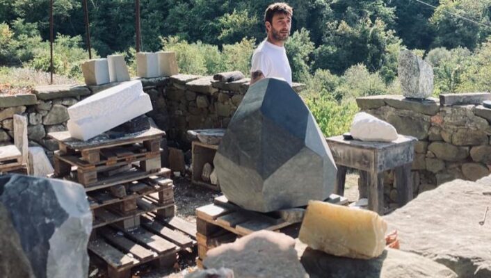 sculptor Lorenzo Brinati standing on a hillside around large pieces of rocks he's going to sculpt