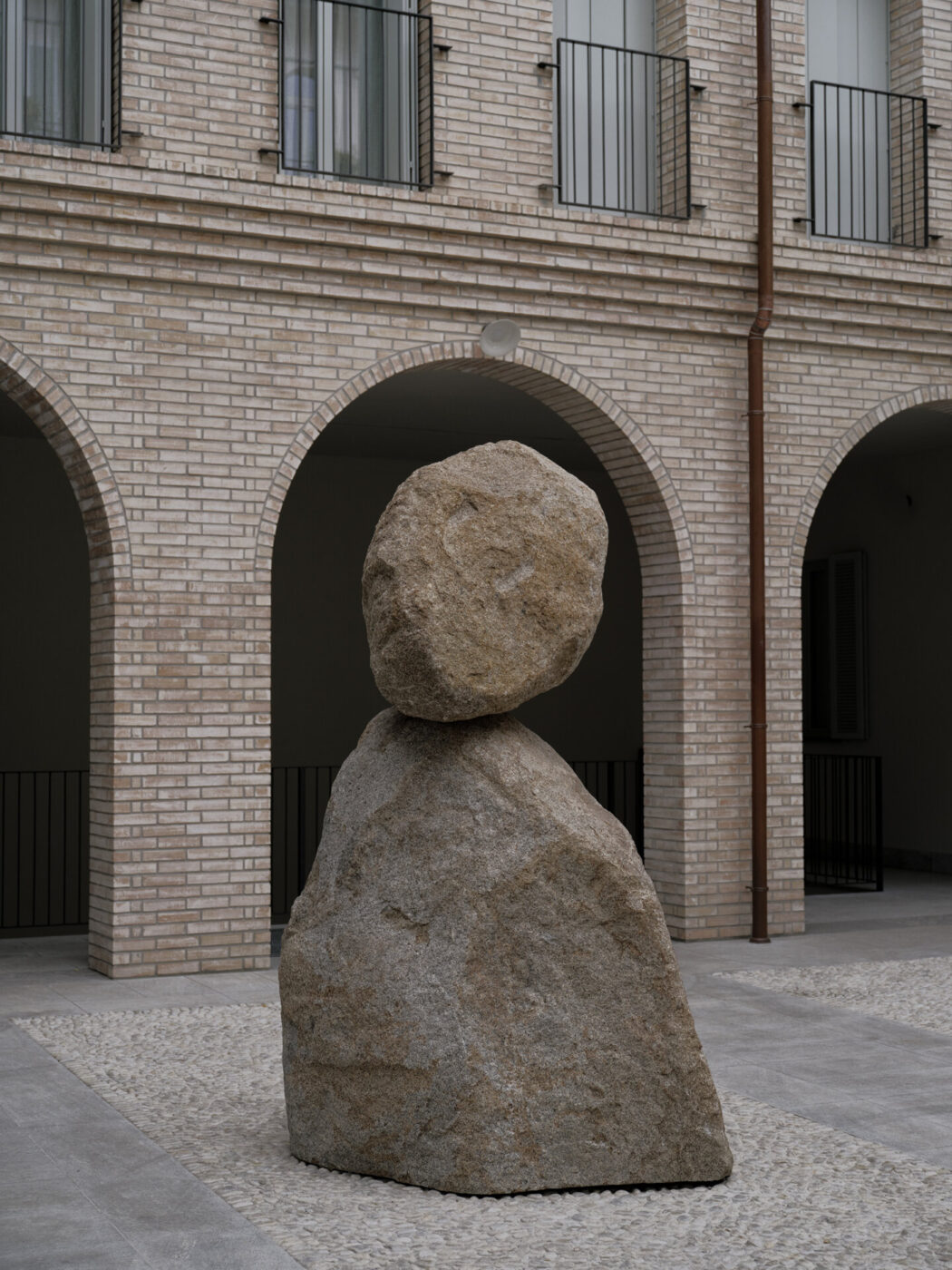 a sculpture by Lorenzo Brinati of a circular rock on a more triangular rock in a courtyard of brick arches