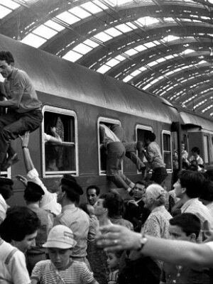 a black and white image of a crowded train in Milan with people climbing into the windows from ferragosto 1970