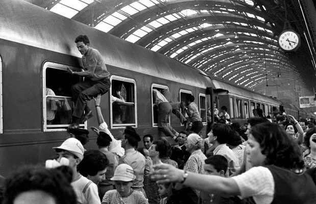 a black and white image of a crowded train in Milan with people climbing into the windows from ferragosto 1970