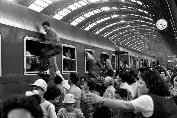 a black and white image of a crowded train in Milan with people climbing into the windows from ferragosto 1970