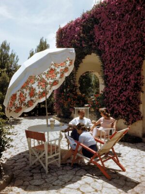 a photo of capri in 1949 by Ralph Crane: three people sitting at a table with a floral umbrella in front of a purple bougainvillea covered wall