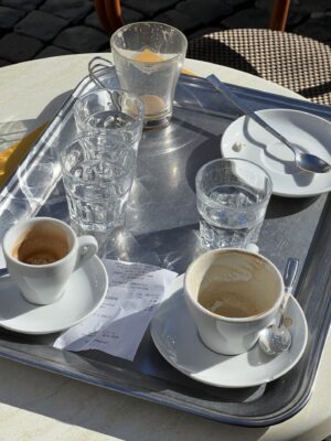 a silver tray out in the sun with three empty espresso cups and three water glasses and receipts