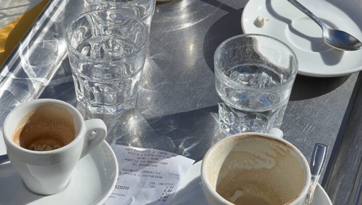 a silver tray out in the sun with three empty espresso cups and three water glasses and receipts