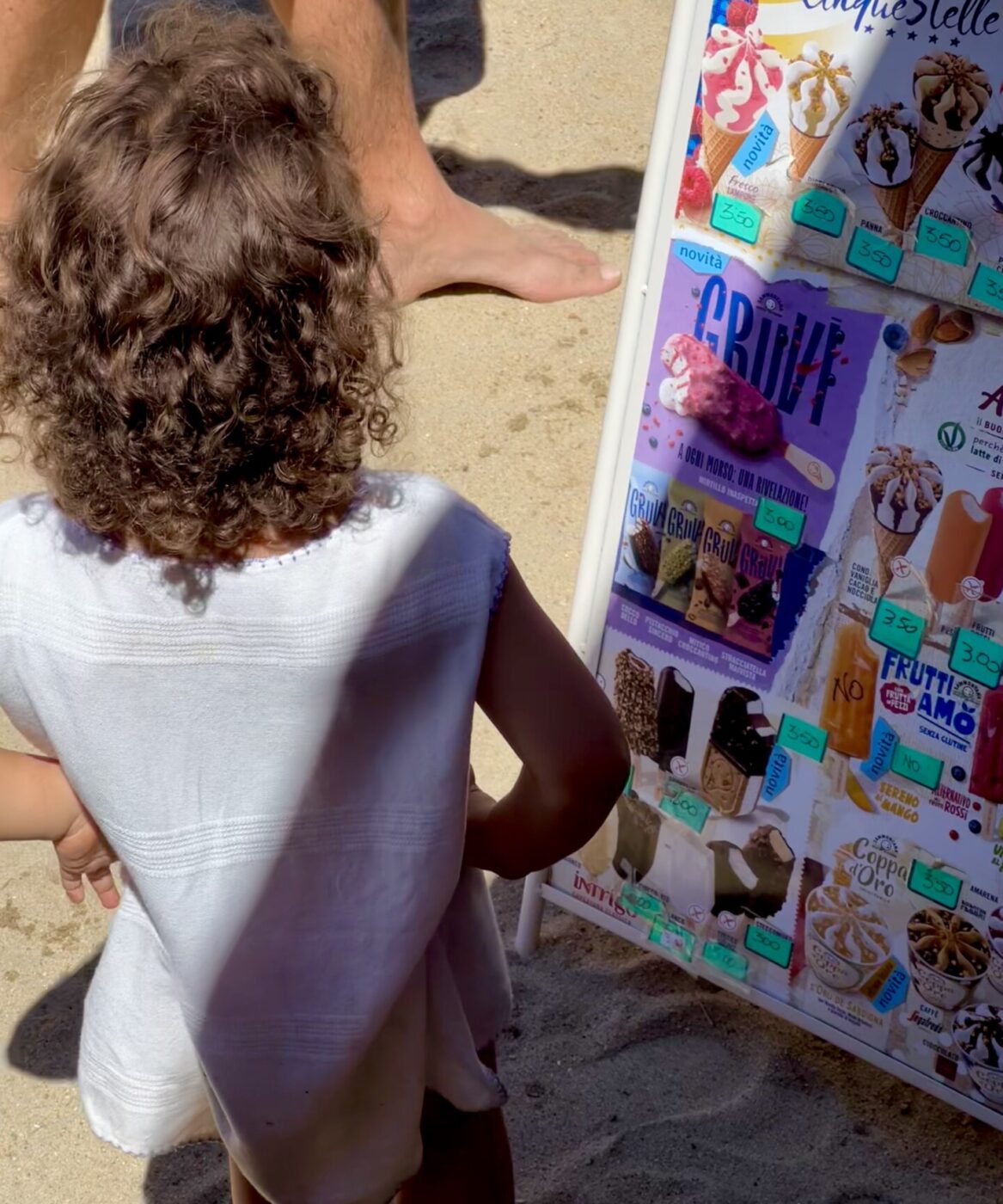 the back of a little girl standing by a sign advertising gelati confezionati